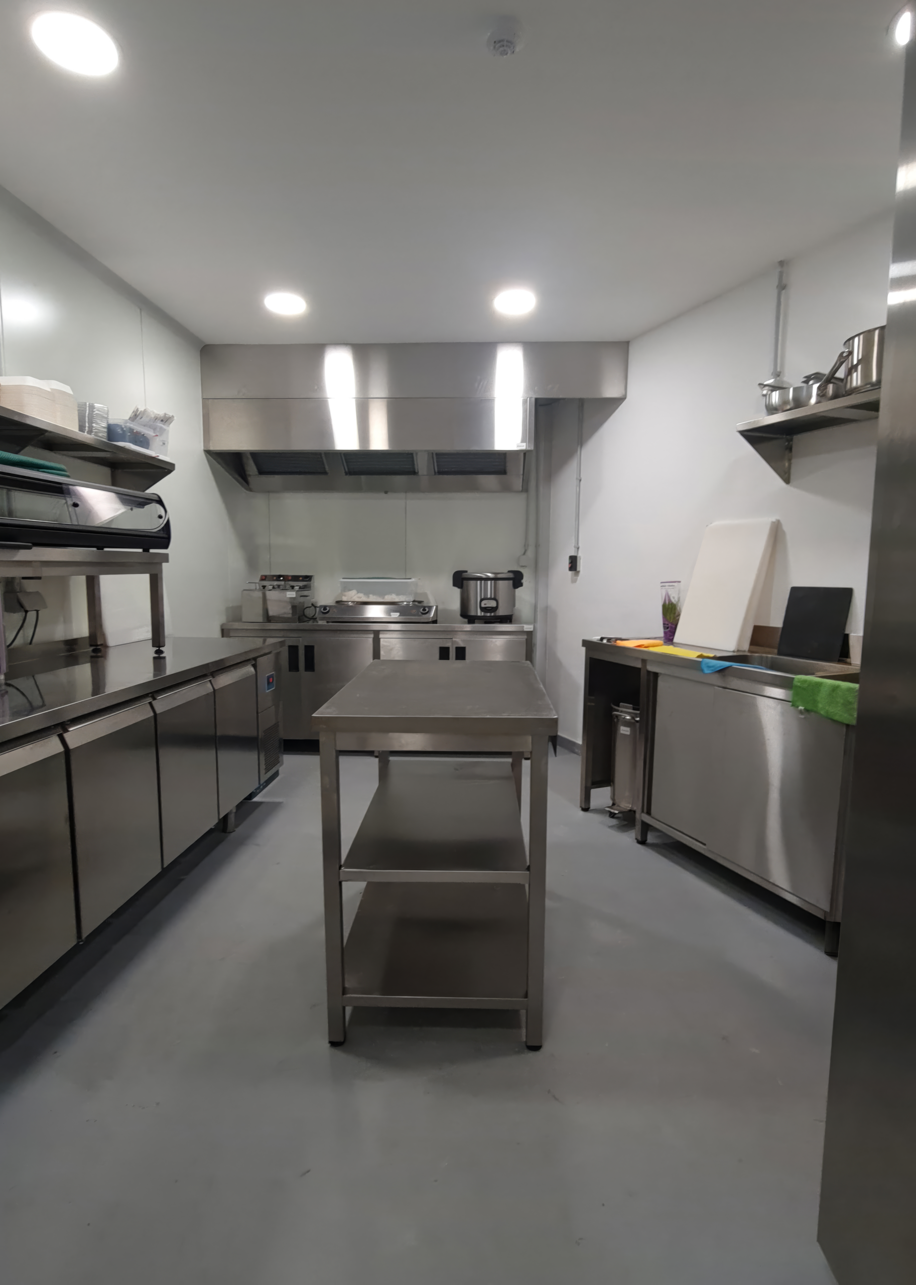 Cozinha profissional privada com bancadas em aço inoxidável, mesa de preparação central e exaustor