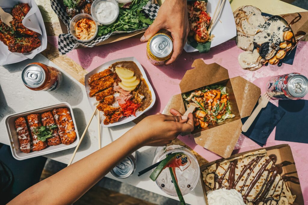 Mesa com diversos pratos de comida de rua, bebidas e mãos a partilhar a refeição
